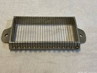 Top side view of rectangular metal cheese slicer with wire cutters and two side handles.