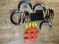 Top view of all track pieces including black curves with flames, straight sections, orange fan unit, yellow supports, and blue car on wood floor.