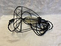 Photo showing the wire cage lamp with attached textile cable and on/off toggle switch lying on a white surface, with a visible filament bulb inside the cage.