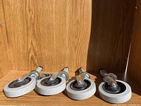 Four dolly wheels laid side-by-side showing tread and mounting bracket on wooden background.