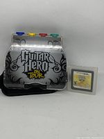 Silver Guitar Hero On Tour grip accessory and yellow-labeled game cartridge for Nintendo DS shown side by side