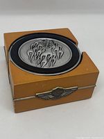 Set of four metal chrome Harley-Davidson coasters with flame design stacked in a brown wooden holder with Harley-Davidson 100th anniversary emblem on front.