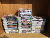 Front view of stacked Xbox 360, PS3, and PS2 video game cases showing titles and condition.