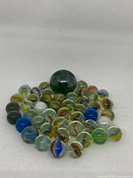 Full view of the lot showing a large green marble surrounded by 43 smaller multicolored glass marbles with inside swirls.