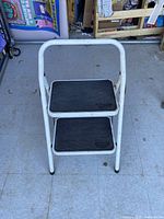 Front view of the metal step ladder featuring two black rubberized steps and white painted metal frame.