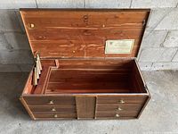 Open cedar chest showing interior wood and Heirloom Chests label inside lid with fluted wood panel front and brass hardware.