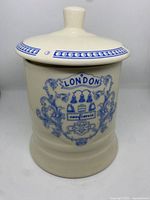 Front view of vintage cream ceramic confiserie jar with blue 'London' design and lid on