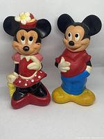 Photo of the two vintage Disney shampoo bottles of Mickey and Minnie Mouse standing side by side on a white surface.