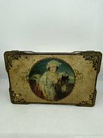 Front view of vintage tin box showing the painted image of a woman with a horse and ornate corner decorations