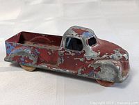 Side view of 1940s metal toy truck showing worn red and blue paint and flatbed at rear