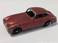 Side view of vintage Aston Martin die-cast car showing significant paint chipping on roof, doors, and front fender.