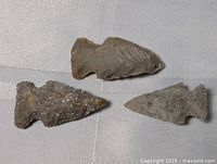 Three flint arrow and spearheads arranged on a white textured fabric background