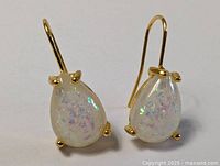 Pair of gold plated earrings with teardrop-shaped opalescent stones set in gold prongs, shown front-facing with hooks visible.