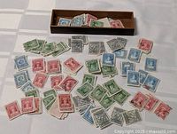 Wood surface with large assortment of loose Newfoundland stamps in red, green, blue; mix of denominations and conditions including cancellations.