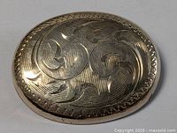 Close-up image of the oval sterling silver brooch with carved decorative pattern showing front side.