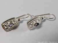 Pair of sterling silver earrings with oval amethyst stones and decorative silver detailing laid flat on a white background.