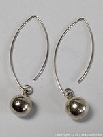 Photo showing pair of silver earrings with ball drops against a white background.