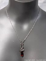 Front view of the sterling silver necklace displayed on a black mannequin, showing the pendant with a deep red garnet gemstone and silver charms.