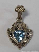 Front view of vintage sterling silver pendant featuring a triangular faceted blue topaz stone set in an ornate silver frame.