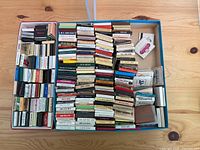 Top-down photo of a large box filled with a diverse collection of matchbooks and matchboxes arranged neatly showing different colors and some logos.