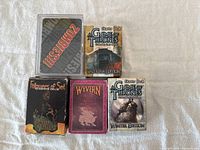 Five assorted starter decks and card game boxes displayed on a white surface. Decks include two Game of Thrones Winter Edition starter decks, one Followers of Set starter deck, one Wyvern expansion, and one Zombie Dice deck.