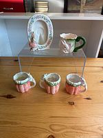 Photo showing all cups and the oval plate with bunny figurine on display stand, depicting full set