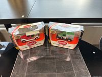 Two Coca Cola model delivery trucks in unopened Matchbox Collectibles packaging with visible Coca Cola branding and 50th anniversary badge.