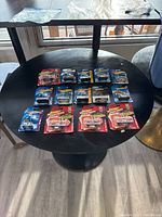 Overview photo showing a total of 14 diecast cars in packaging, arranged on a round table including both Johnny Lightning and Hot Wheels brands.