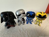 Four loose Funko Pop vinyl figures placed side-by-side: Darth Vader, silver armored Star Wars character, blue and yellow Power Rangers.