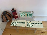 Five items displayed: leather helmet, red commemorative decanter, license plate, two stickers.