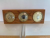 Full view of the wooden mounted vintage weather station featuring three dials for hygrometer, barometer, and thermometer.