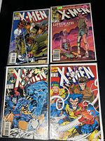 Four 1980's X-Men comic books laid out on a black surface. Covers show various X-Men characters in illustrated action scenes. Titles and issue numbers visible.