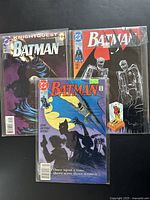 Three vintage Batman comic books including Knightquest: The Crusade, a comic with a black cover showing two skeleton-like figures in Robin costumes, and a comic featuring Batman with the text 'Once upon a time, there were three women'.