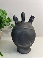 Front view of black pottery jug vase showing three spouts and incised diamond pattern detailing.