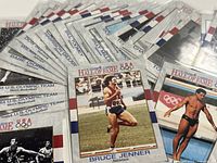 Close-up photo showing multiple Olympic trading cards with Bruce (Caitlyn) Jenner card prominent, cards sleeved in plastic protectors, various athletes' names visible on cards.