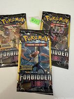 Three unopened booster packs from the Pokemon Sun & Moon Forbidden Light series, showing front artwork with Greninja, Decidueye, and Silvally.