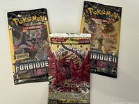 Front view of three unopened booster packs: two Pokémon Sun & Moon Forbidden Light and one Yu-Gi-Oh! 5D's Crossroads of Chaos pack.