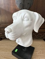 Front angled view of white dog head sculpture on black base, showing textured nose and detailed facial features.