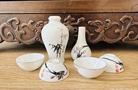 Photo showing two Chinese porcelain vases and four matching small bowls with hand-painted black bamboo and red seals on a wooden surface.