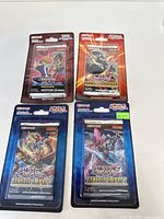 Four sealed Yu-Gi-Oh! trading card booster packs including two Genesis Impact packs and two older series (Antique Gear and Duelist Chronicles) packs arranged on a white background.