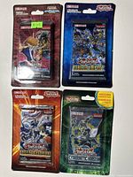 Four unopened Yu-Gi-Oh trading card booster packs laid out showing front artwork with different themes and colors.