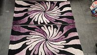 Top view of two carpet runners side by side showing a swirling floral design in purple, white, pink, and black colors.