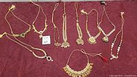 Full view of the 10 assorted costume jewelry necklaces laid on burgundy fabric