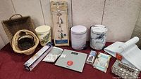 Full set of household accessories showing baskets, waste bin, scale, organizers, and cleaning items arranged on floor.