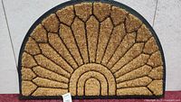 Top view of the door mat showing natural coir fiber surface arranged in a segmented fan design with black rubber border.