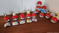 Set of eight Pokemon Collector Balls lined up on a wooden surface with various Pokemon figures on top each ball and their respective cards placed in front.