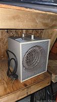 Front side view of the Heron Cable portable heater showing metal mesh grille, handle on top and power cord coiled beside it.