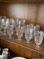 Four groups of stemmed crystal glasses in 4 different shapes and sizes arranged in rows on a wood shelf, totaling 32 pieces.