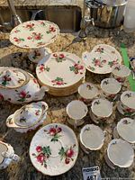 Full set of Hammersley plates, cups, saucers, cake plate, teapot, creamer, and sugar bowl with red rose pattern and gold trim displayed on countertop.