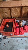 Multiple red plastic jeri cans, brown oil containers, and a red plastic storage container with a small can inside